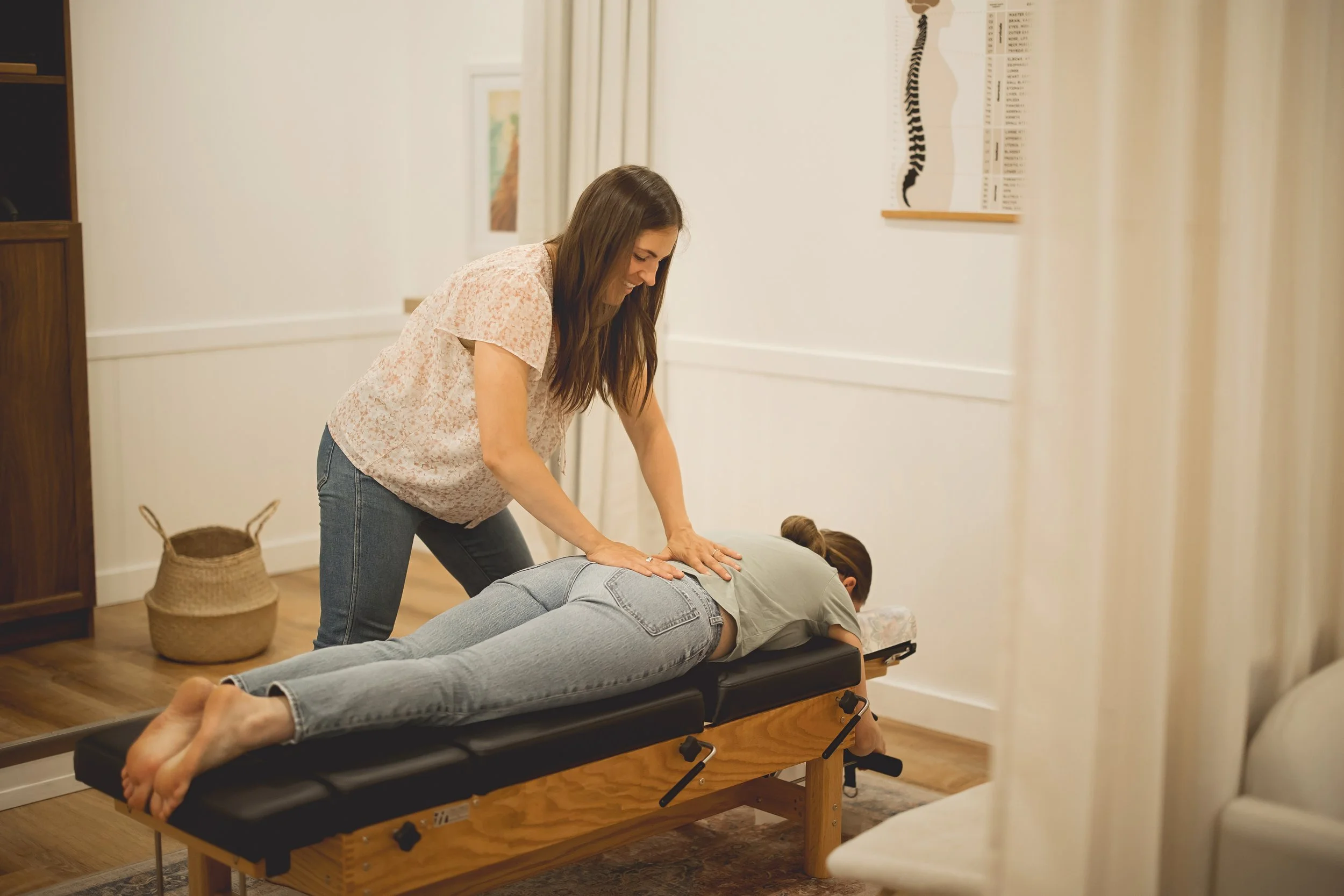 A woman providing chiropractic care to a young girl lying face down on a treatment table.