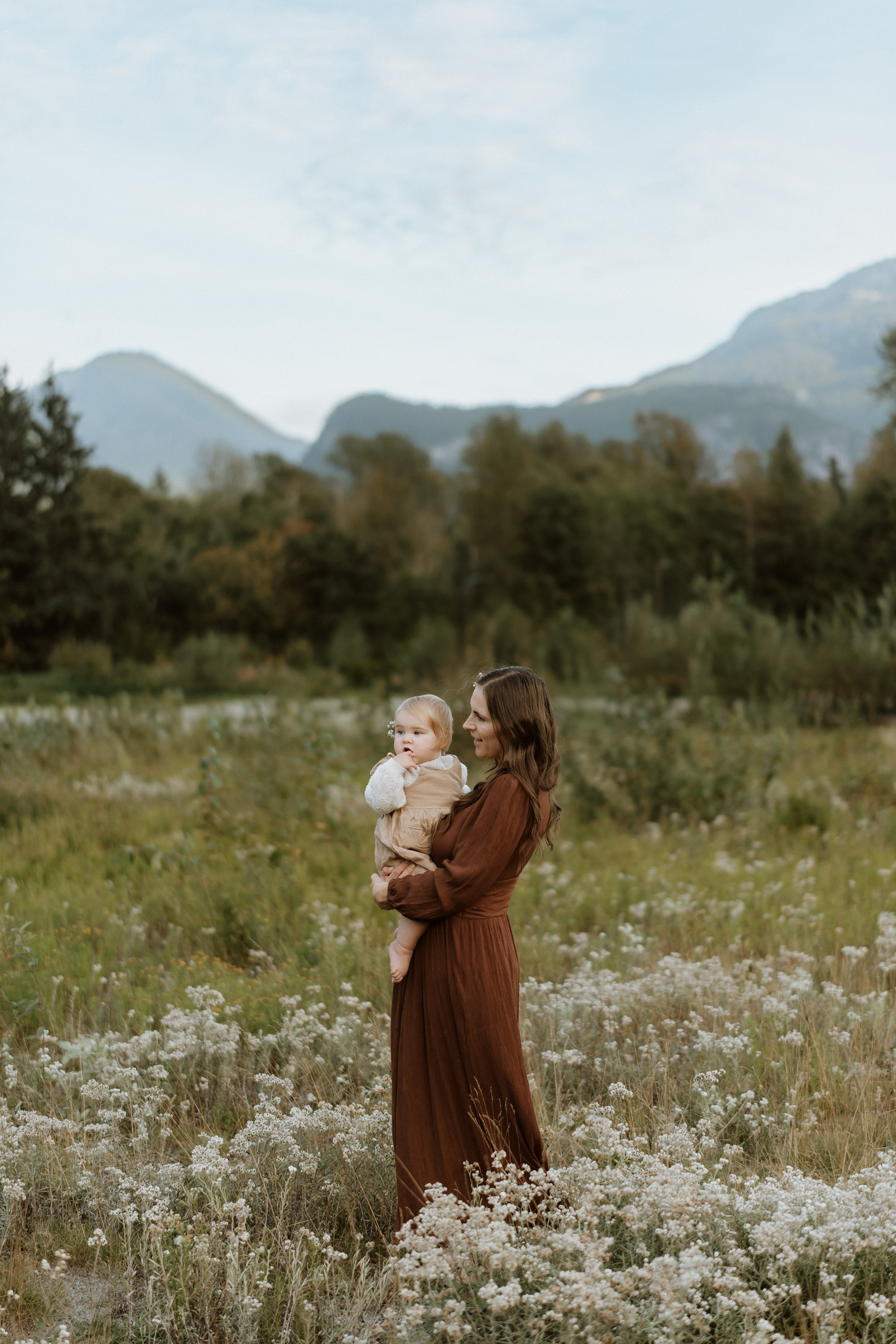 A woman holding a young girl in a field of white flowers with mountains in the background.