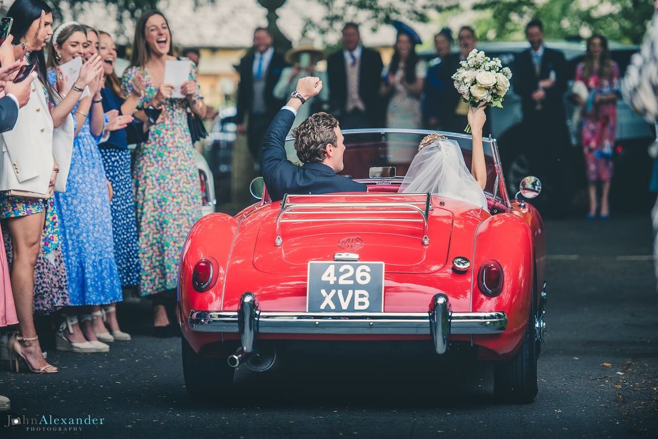 COTSWOLD WEDDINGS 
Picture-perfect moments as the newlyweds drove away from their church ceremony in the Cotswolds, embracing the charm of yesteryears in a vintage red racing car. 
Wedding Planner: @plannedforperfection 
Photographer: @jeaphotography