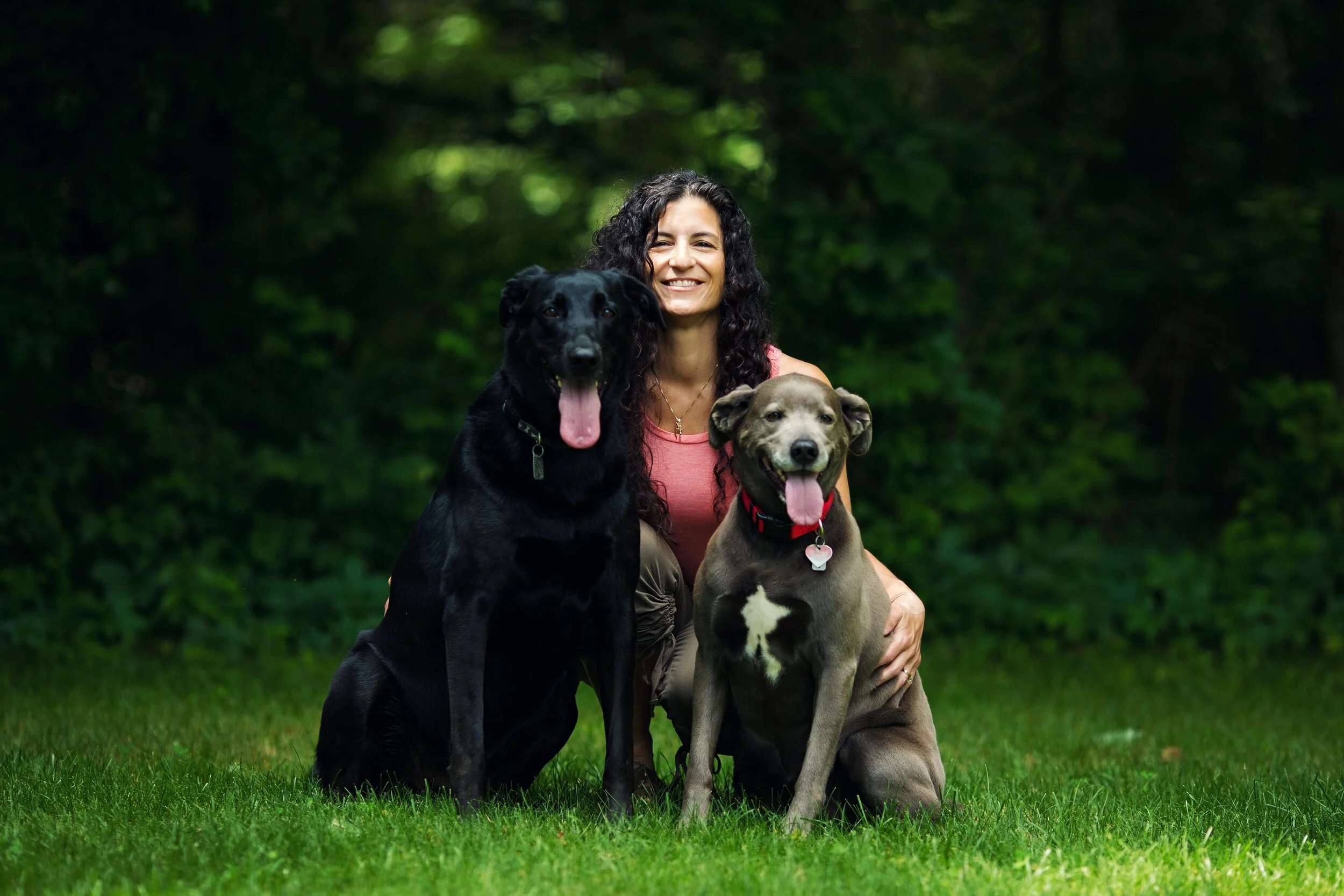 Janine kneeling in a field with her two dogs, Zoey and Dakota