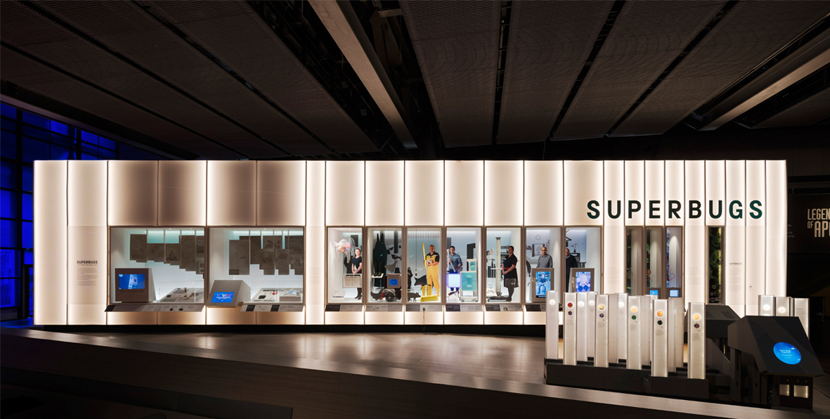 SUPERBUGS, The Science Museum London, UK 2017 EXHIBITION DESIGN The SUPERBUGS exhibition explores antibiotic resistance from micro to macro scale through personal stories. Our exhibition design for The Science Museum challenges the traditional wall sectioned exhibition layout with a 20 meter long illuminated curiosity wall freeing up floor space and utilising existing seating. At the same time it can be approached from either end of the gallery, inviting visitors to come closer. The display wall consists of a transition of narrow to wider display cases recessed into an existing structure. The wall illustrates the story of antibiotic resistance from micro to macro scale and from the abstract form of real bacteria culture, through the personal stories of the people who fight bacteria, to today’s global search for new antibiotics. The recessed display cases contain a mix of everyday objects, films, interactive games, props and back-lit illustrations set up as a scenography to create an environment for each individual story. A collection of real bacteria are “flocked” together in a large bug resembling floor piece allowing visitors to explore them at close hand. Collaborators: Science Museum graphics, Michael Grubb lighting