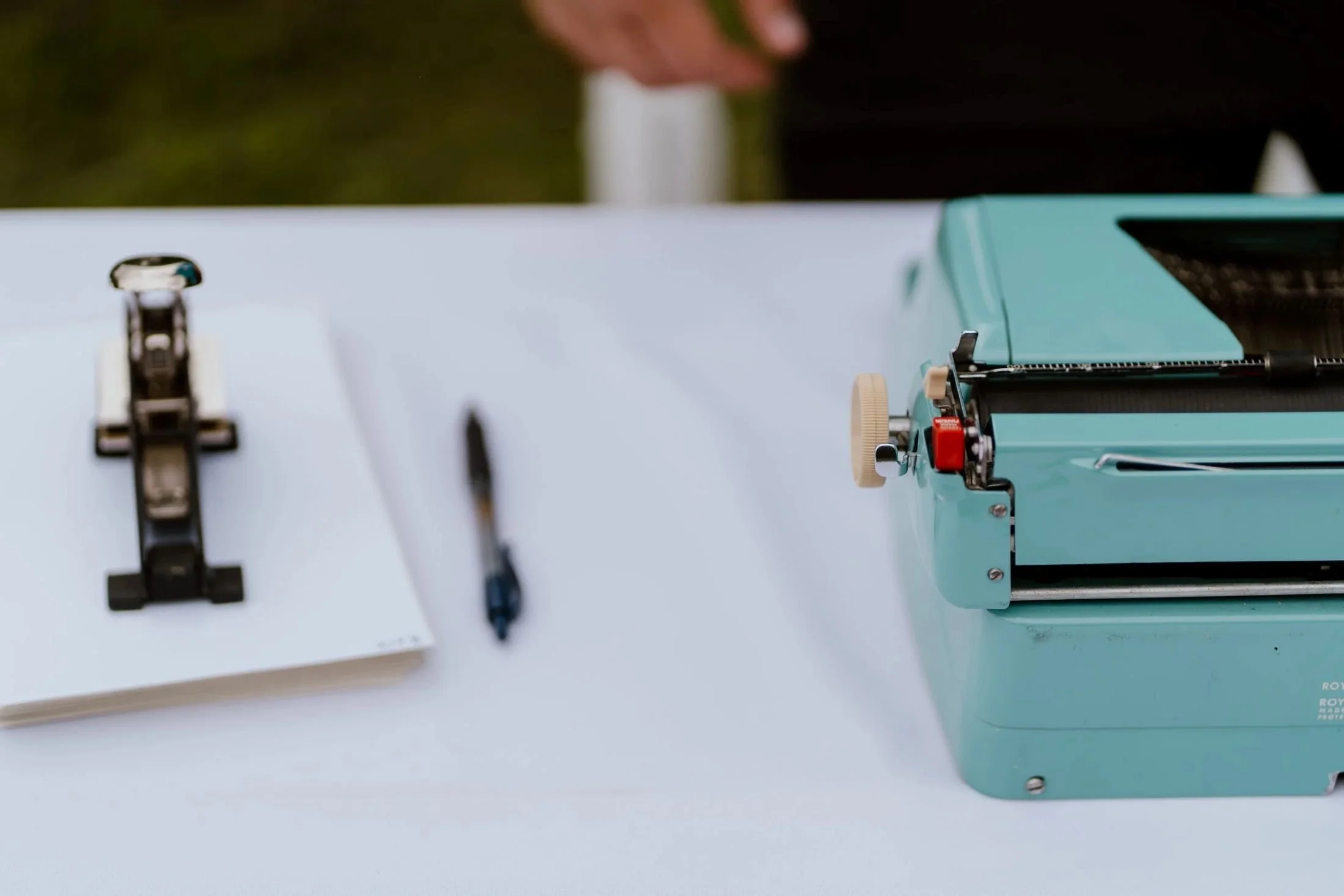 Mark Petersen's teal Royal typewriter for poems on a desk outside at a wedding in a photo by Stephanie Dee Photography.
