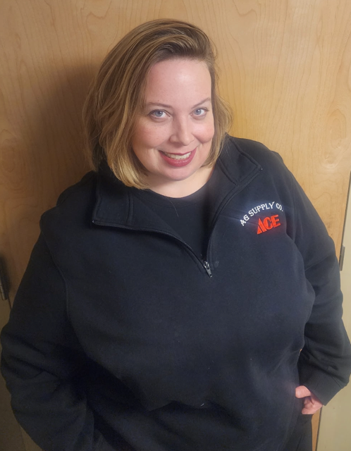 Man wearing glasses and a black and red polo shirt with 'AG Supply Co.' and 'ACE' embroidered on it, standing outdoors with trees and hills in the background.
