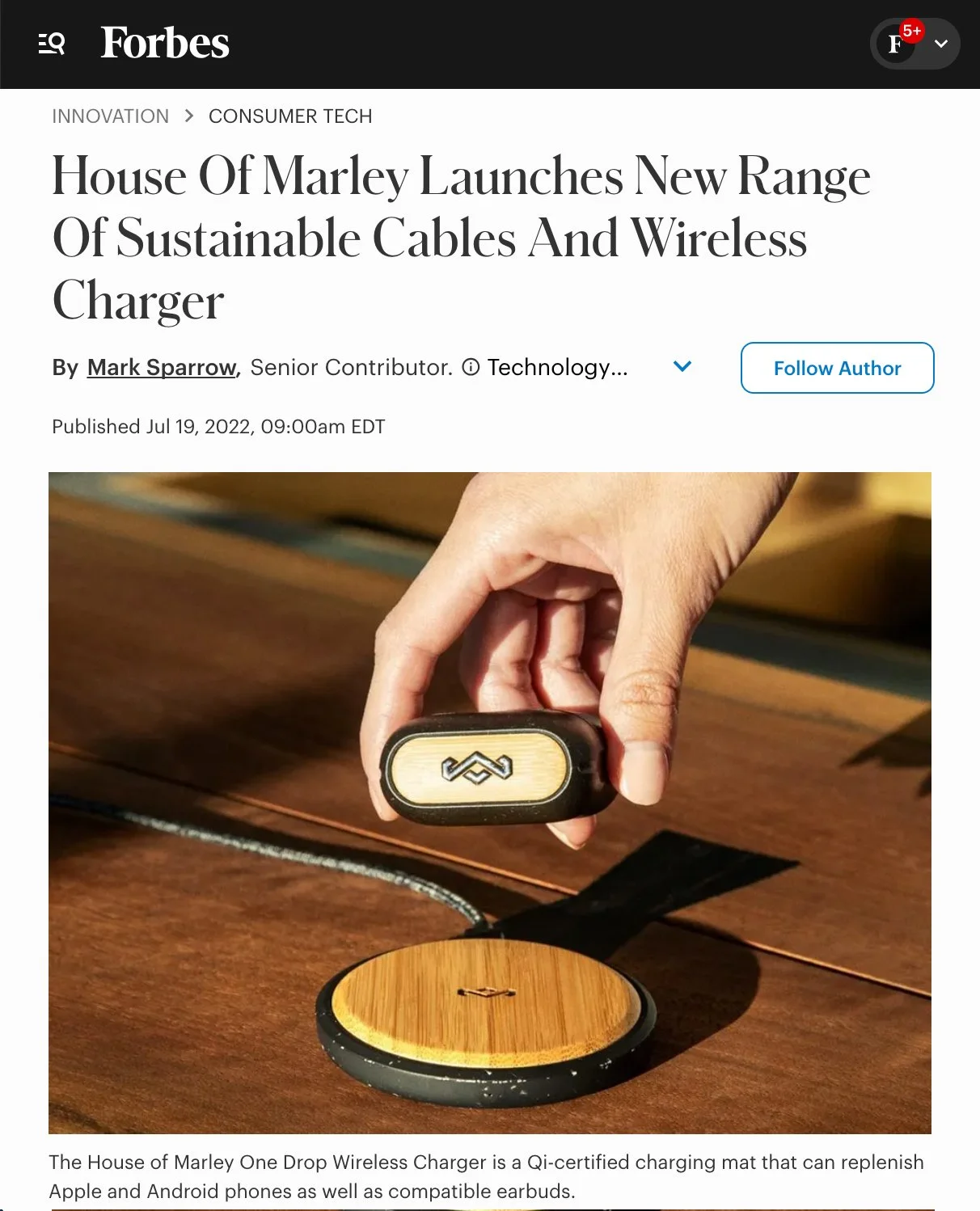 Close-up of a person's hand holding a small wireless charger with a wood finish, placed on a wooden surface.