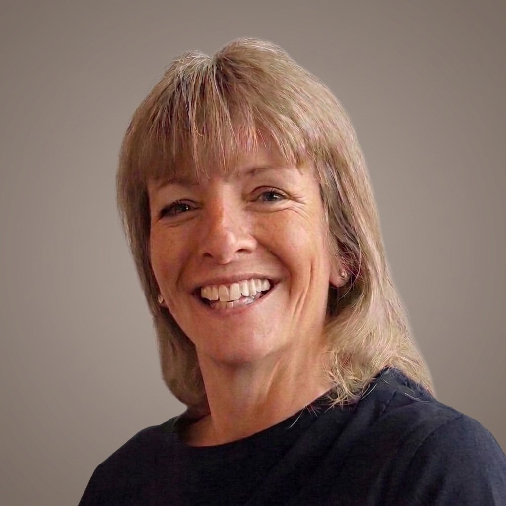 A smiling woman with blonde hair and light skin wearing a black shirt, facing slightly to the left against a plain neutral background.