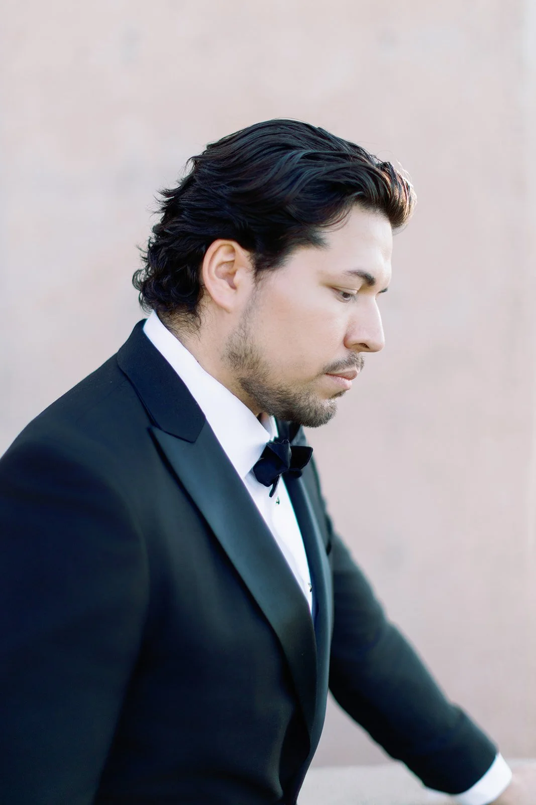 baritone Ethan Vincent dressed in a black tuxedo with a white shirt and black bow tie looking down against a neutral background.