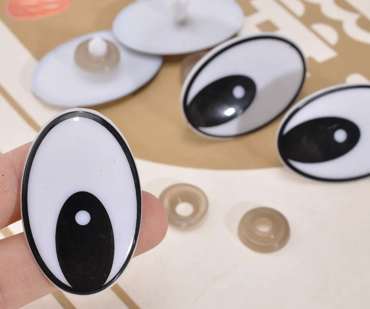 A finger holding an oval black and white eye-shaped object, with several similar eye-shaped objects on a flat surface in the background.