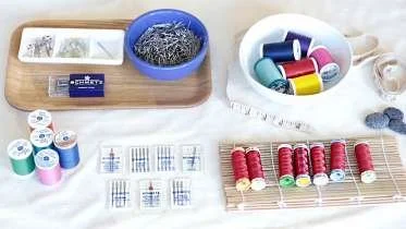 Sewing supplies including small spools of thread, sewing pins in a blue bowl, measuring tape, and fabric swatches.