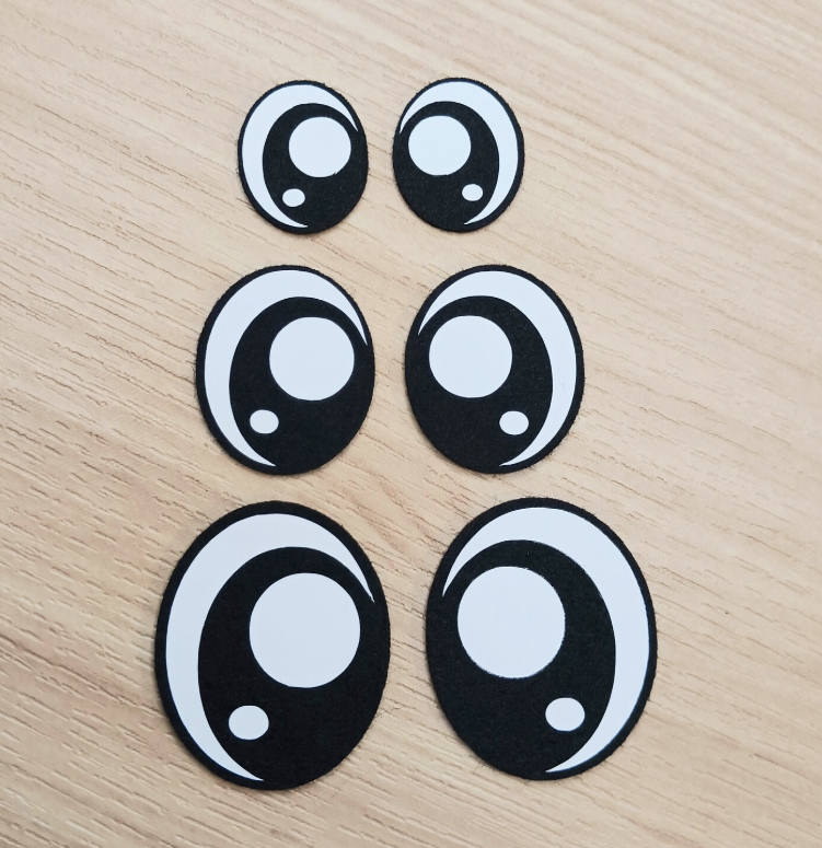 Six black and white cartoon eye stickers of varying sizes arranged on a light wooden surface.