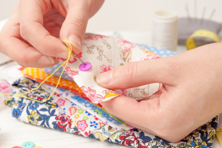 Person sewing fabric with colorful floral patterns using a yellow thread and a pink button.
