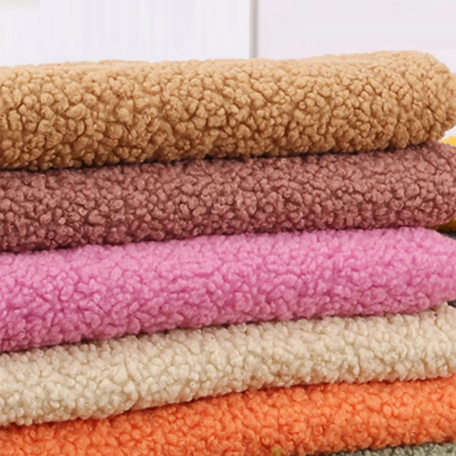 Stack of colorful textured towels in shades of pink, beige, brown, and orange.