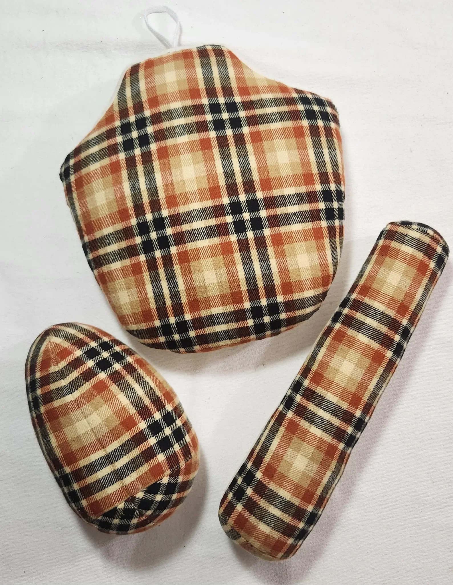 A plaid-patterned face mask, headband, and hair scrunchie in beige, black, orange, and red colors on a white surface.