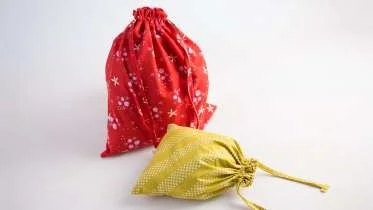 Two small drawstring gift bags, one red with white snowflake patterns and one yellow with white stripes, on a white background.