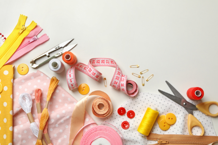 Sewing supplies including scissors, thread, buttons, measuring tape, pins, and fabric on a white surface.