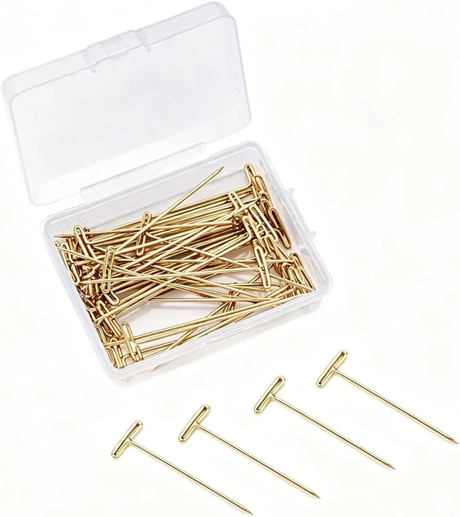 A clear plastic container filled with gold safety pins and four safety pins outside the container on a white surface.