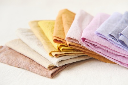 Stacked folded pastel-colored cloths or towels in beige, yellow, orange, pink, purple, and blue