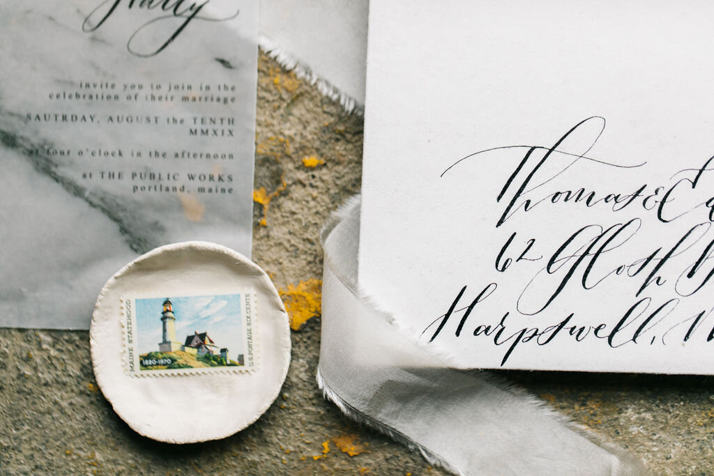 handlettered invitation envelope beside gray wedding invitation and lighthouse stamp