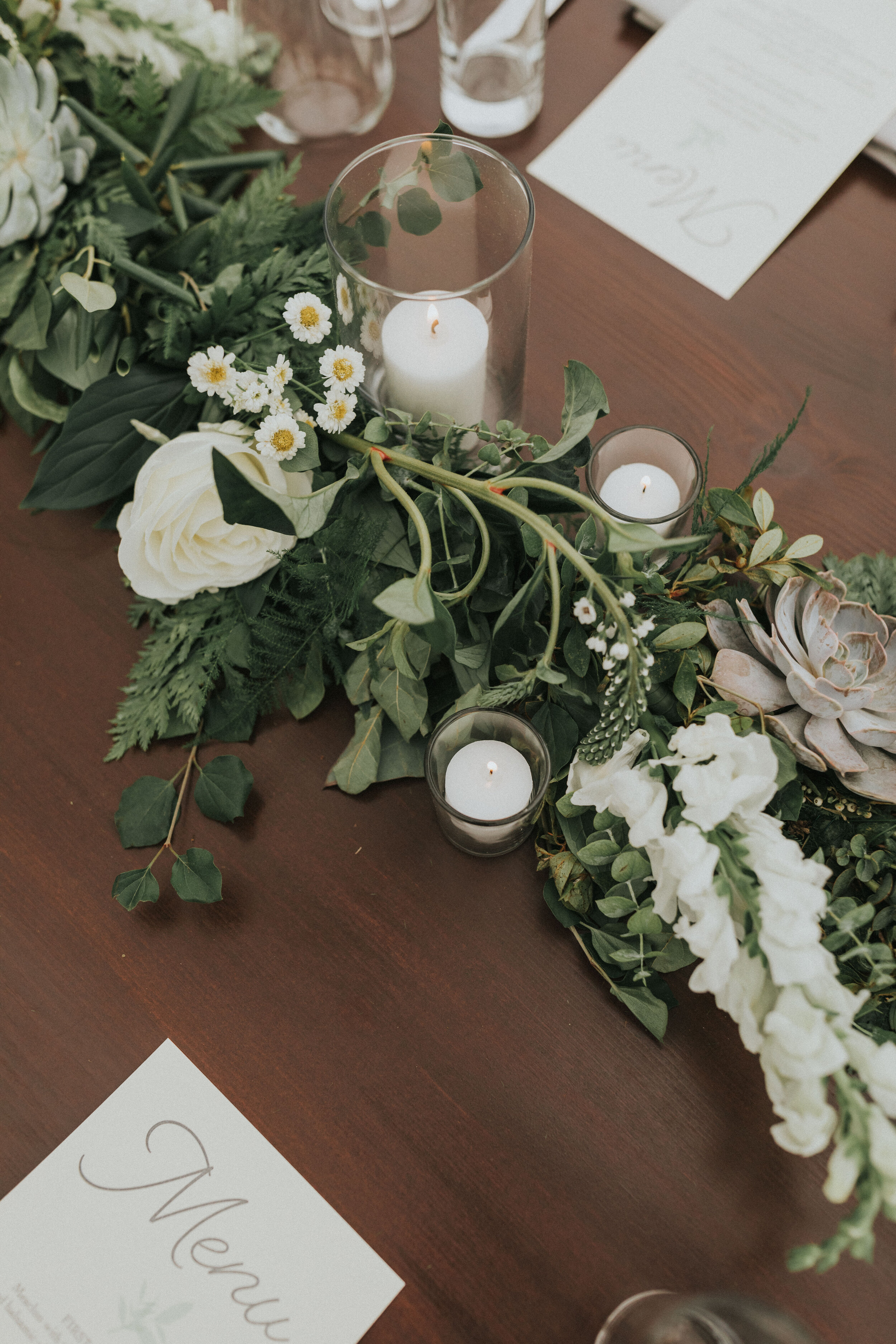 green and neutral floral tablescape beside menu on wedding reception table