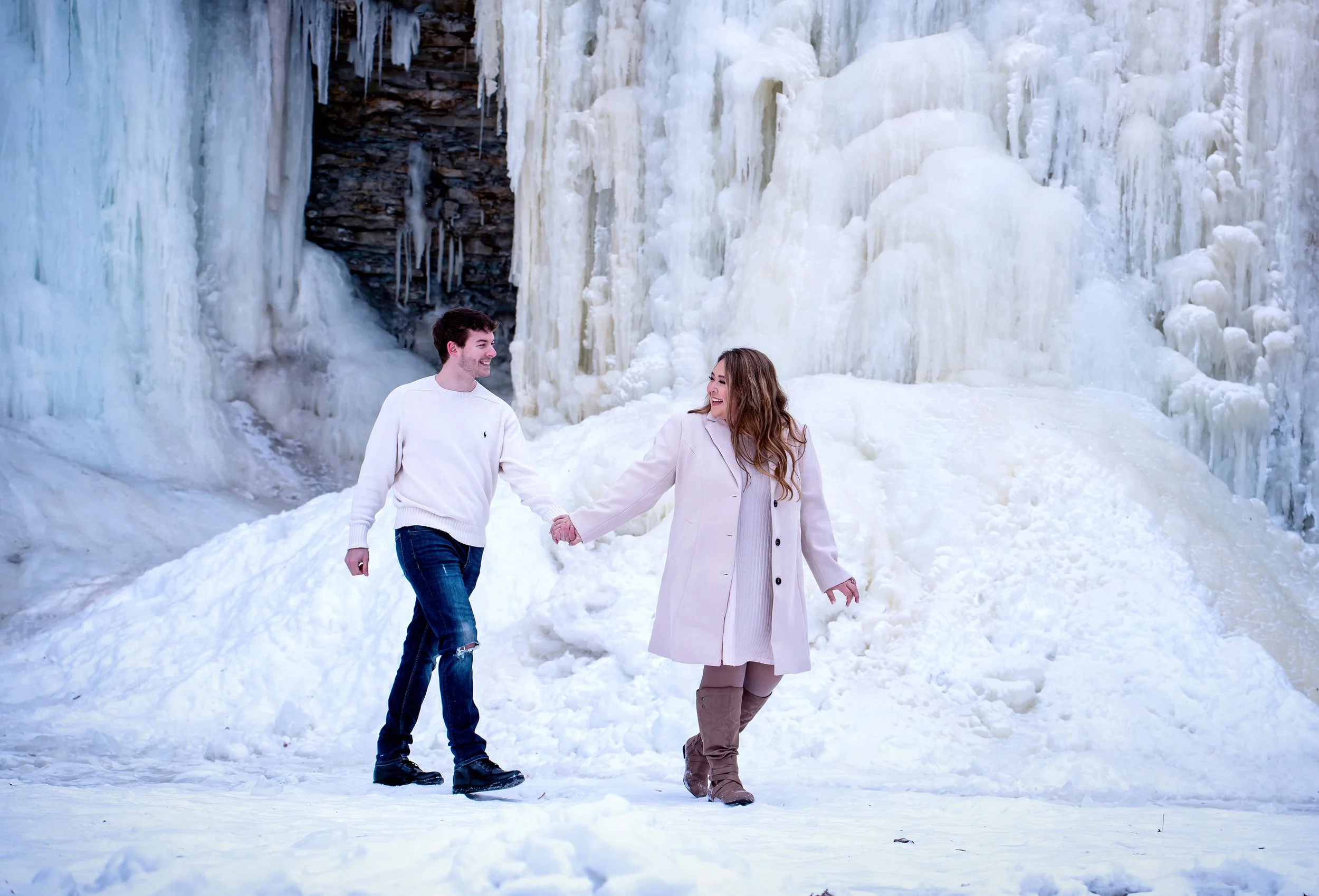 An ethereal winter engagement session takes place at the frozen Wequiock Falls in Green Bay, Wisconsin, where a couple walks hand in hand through a landscape of icy beauty and soft, dreamy light. Captured by AA Studios, these destination photos highl