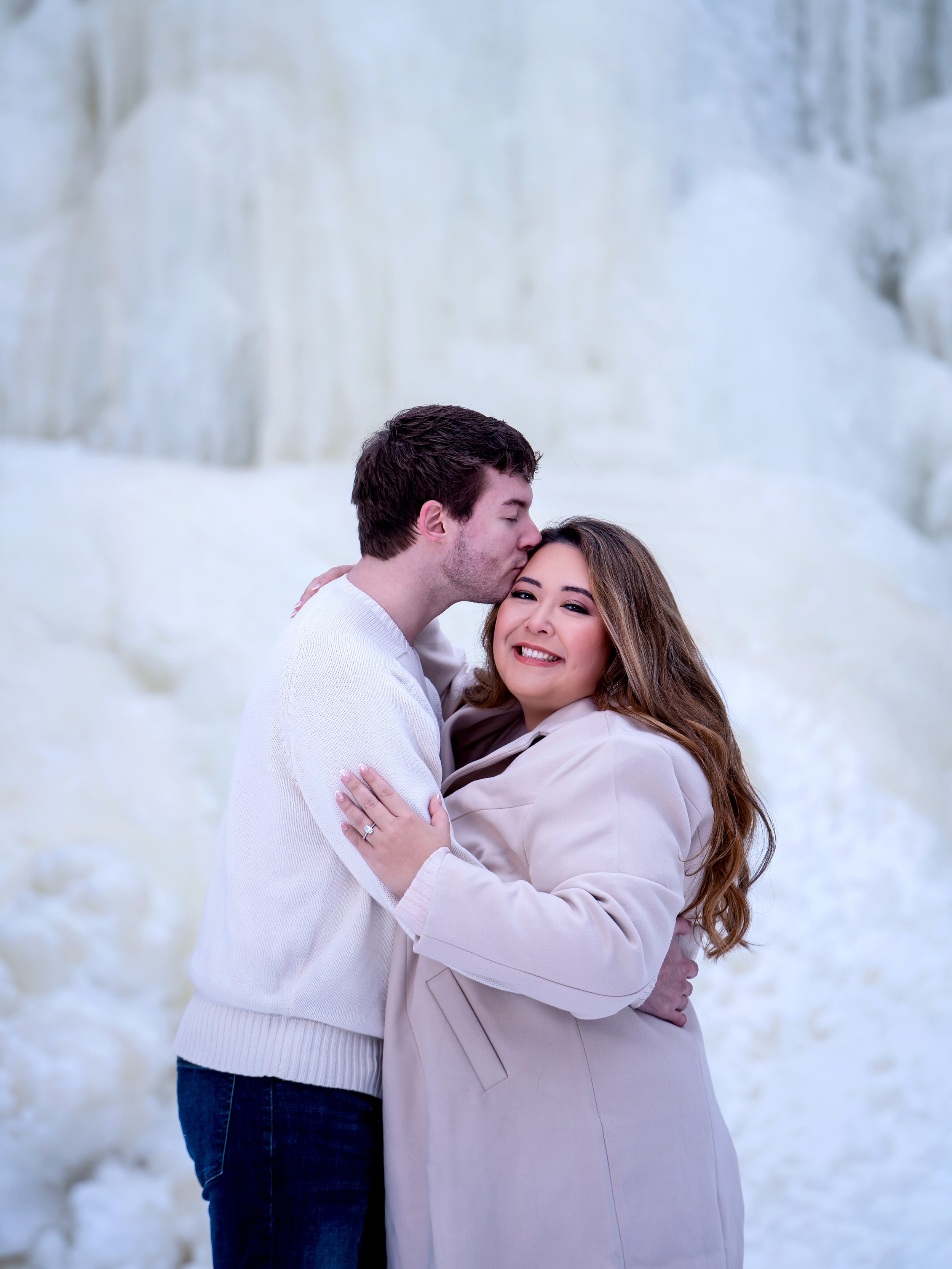 Romantic winter engagement photos of a couple cuddling near frozen Wequiock Falls in Green Bay, Wisconsin, surrounded by dramatic ice formations.