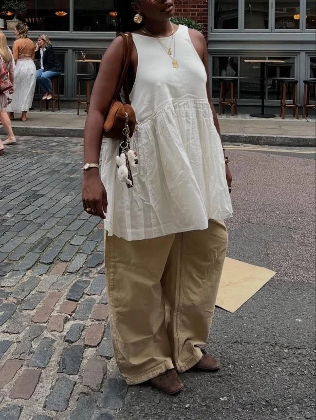 woman in white linen sundress with brown pants on and gold jewellry