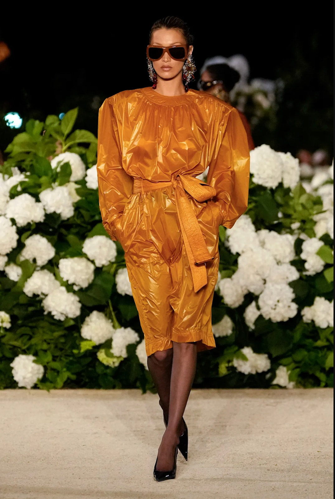 bella hadid on runway wearing 80s inspired orange leather jumpsuit