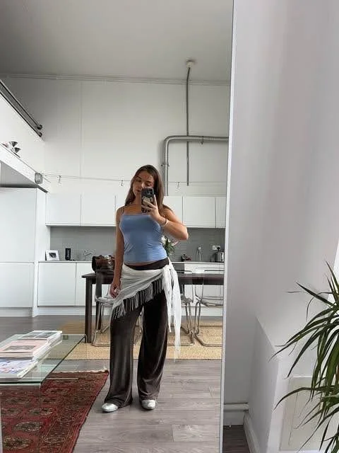 girl taking a mirror selfie of her outfit which features a belt scarf pants and blue top