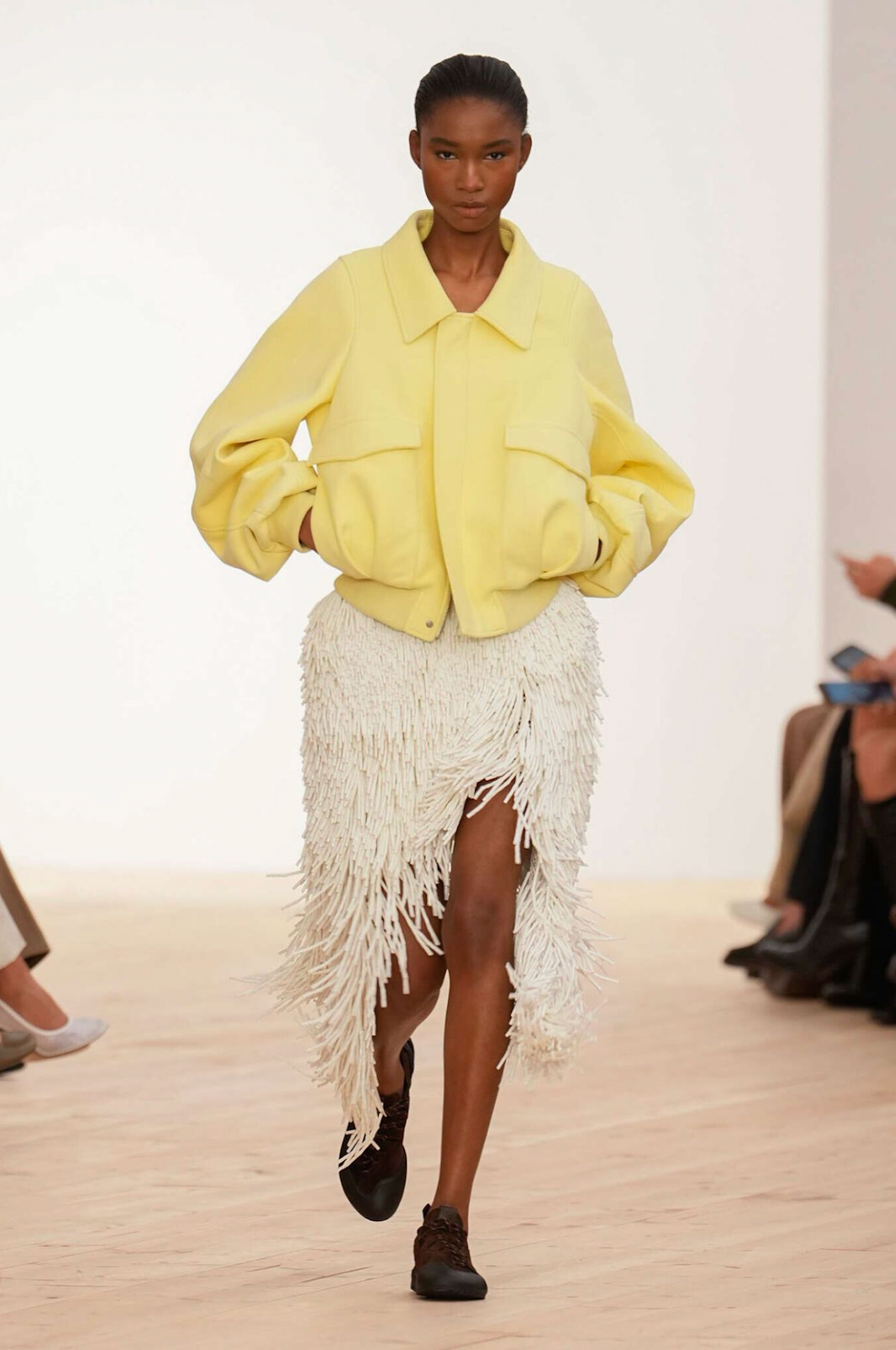 runway model in yellow bomber jacket with white fringe tassel skirt