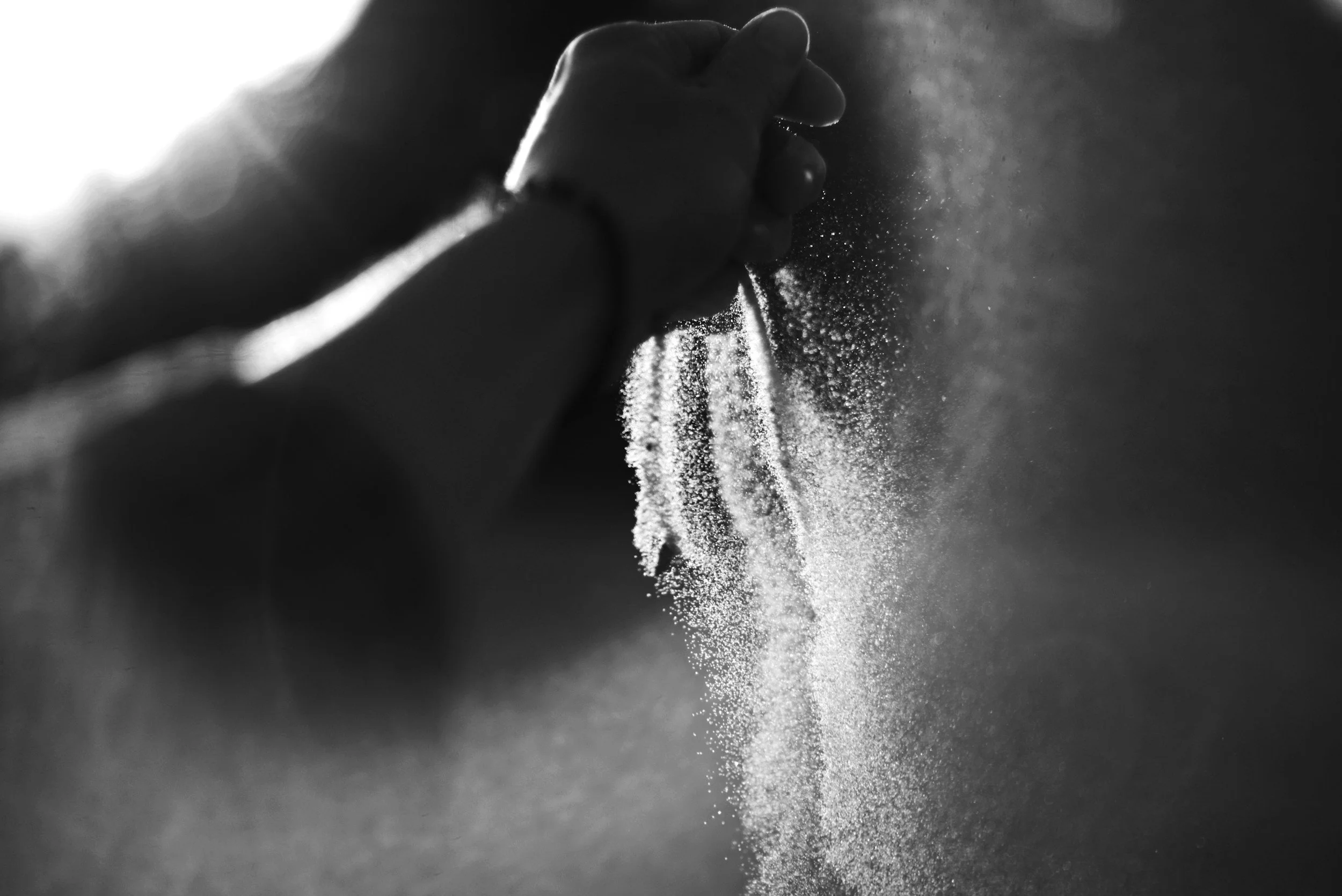 black and white image of a hand releasing a handful of sand