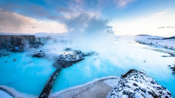 Hot springs in a snowy landscape with steam rising and a wooden walkway.