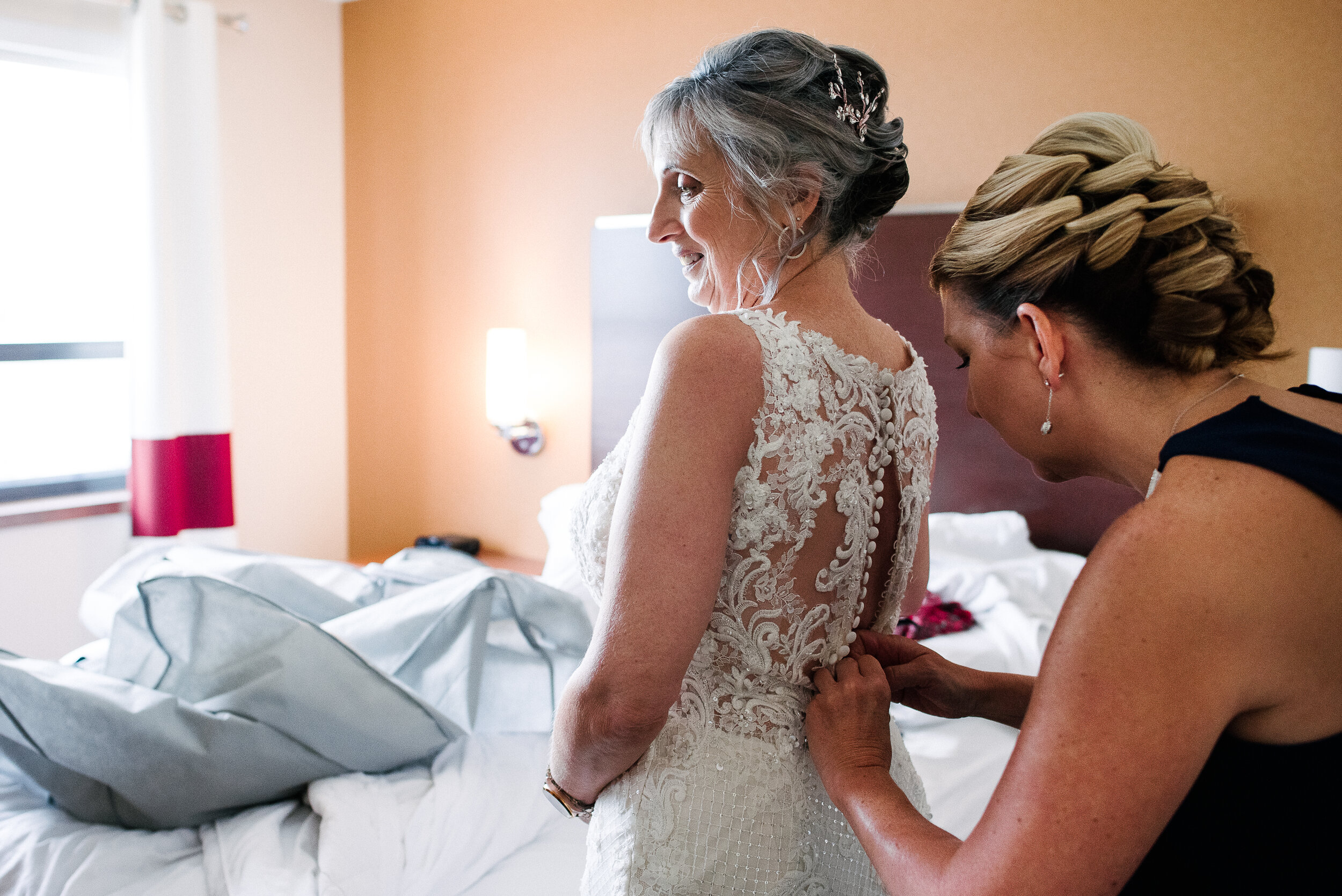 Bridesmaid helping bride dress for wedding in Kingston, Ontario