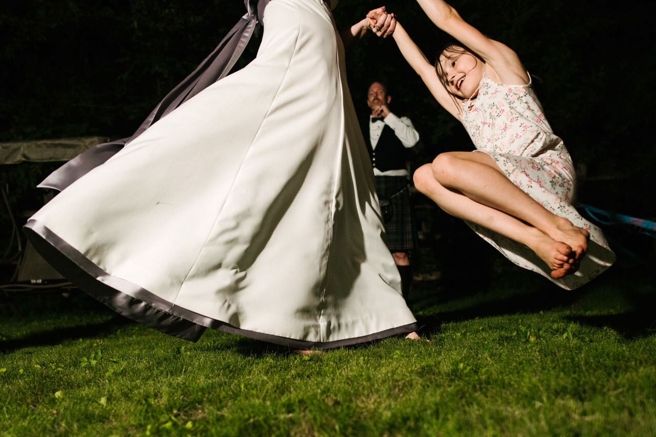 Bride swinging young wedding guest around while dancing at reception 
