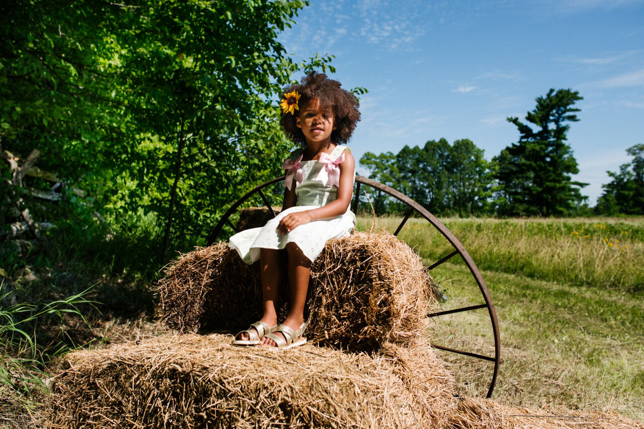 Young girl dressed for a wedding sitting on a hay bale
