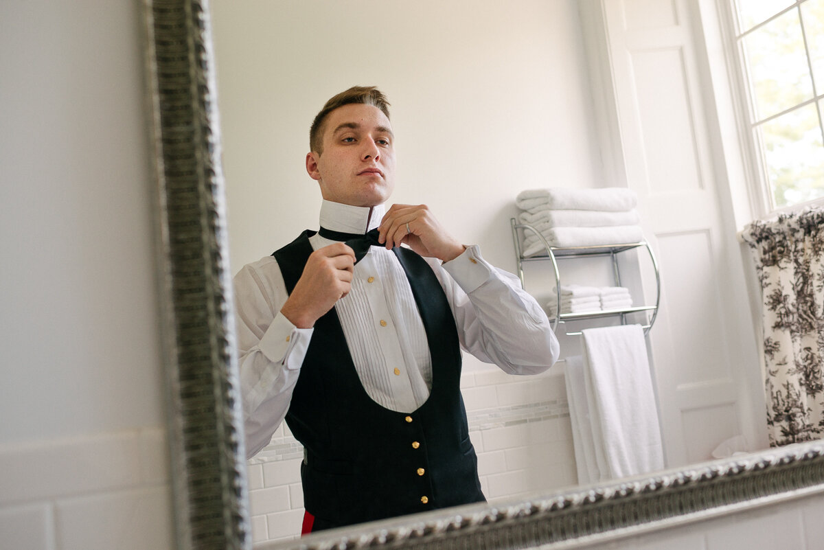 A man adjusting his black bow tie in mirror