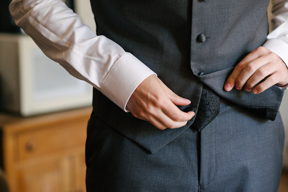 close up of groom putting his vest on 