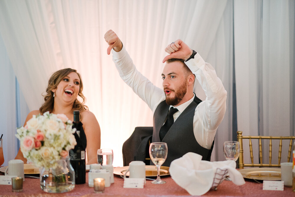 groom laughing and giving thumbs down to a speech during wedding reception 