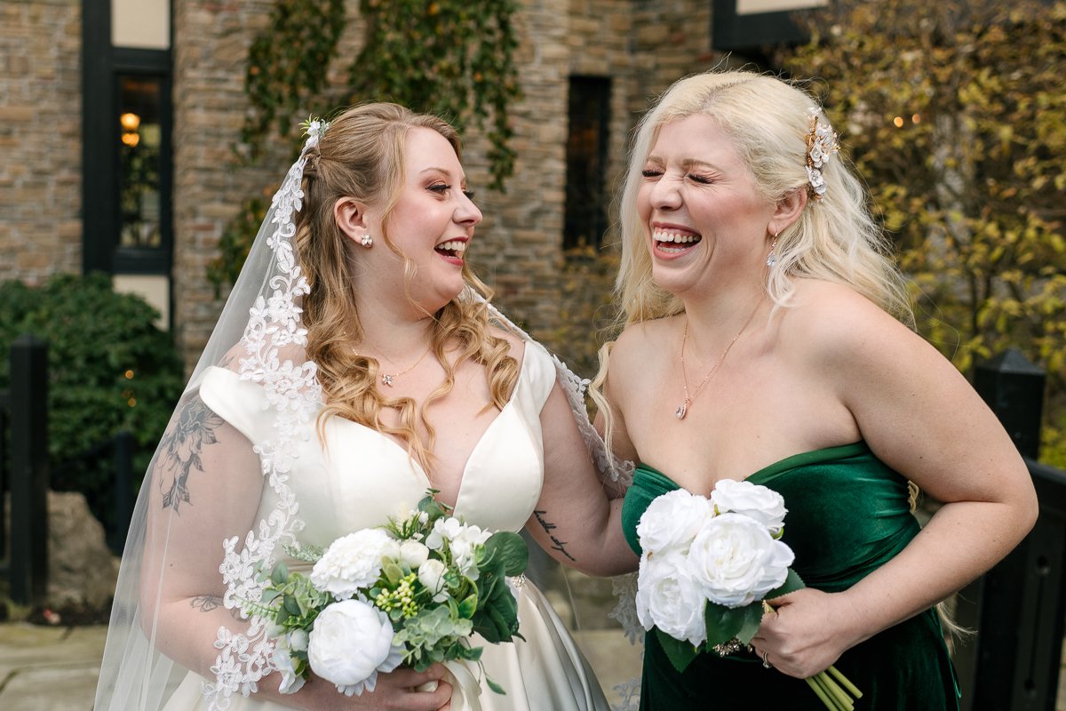 Bride and her friend laughing with joy holding wedding white flowers