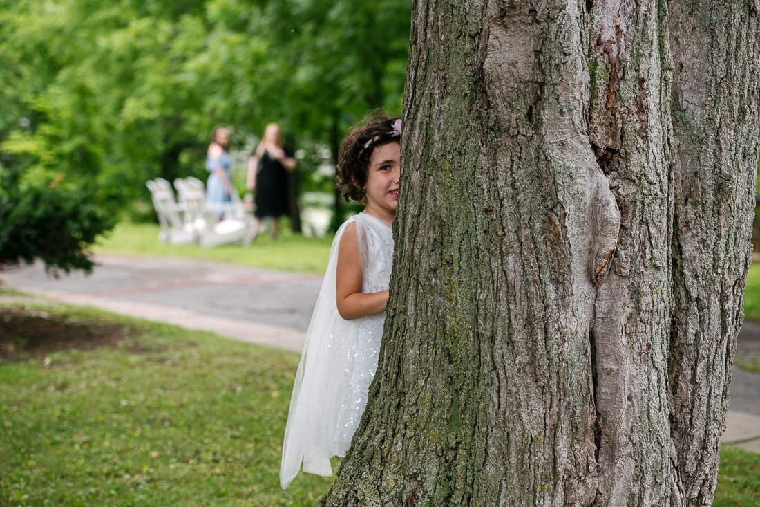 Cute little girl in white dress hiding behind the tree.