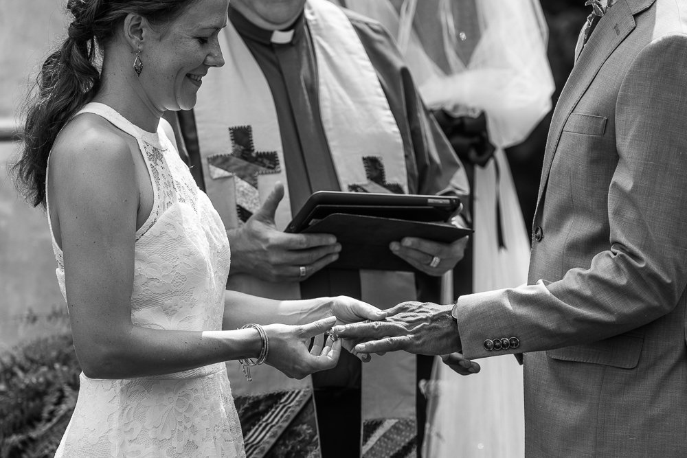 Black and white image of Bride and groom holding each other hands exchanging rings. 