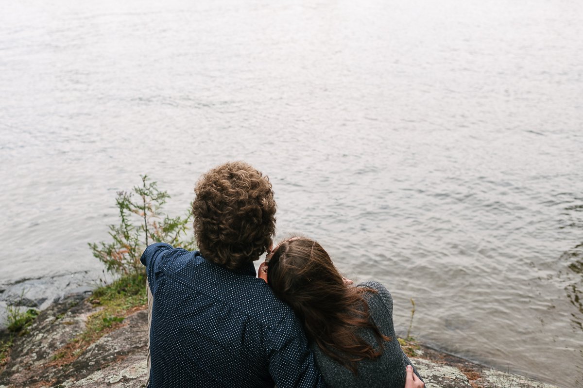 Couple hugging each other sitting near lake.