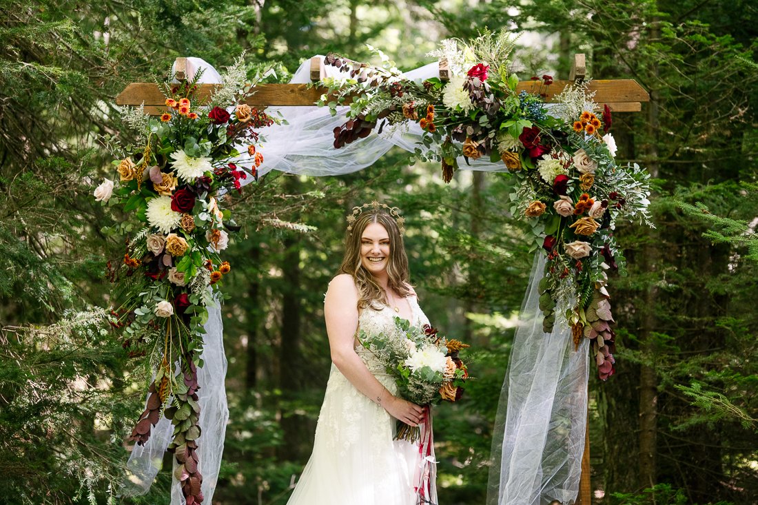 Bride standing under the flower gate with her wedding bouquet