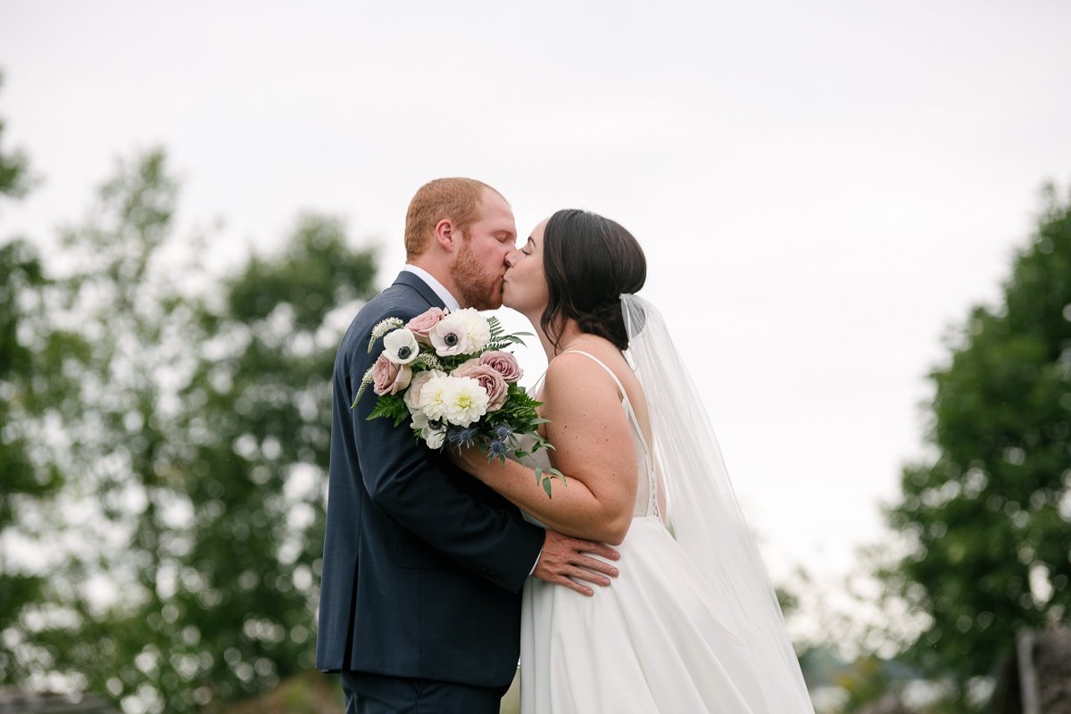 Bride and groom kissing each other holding flower bouquet