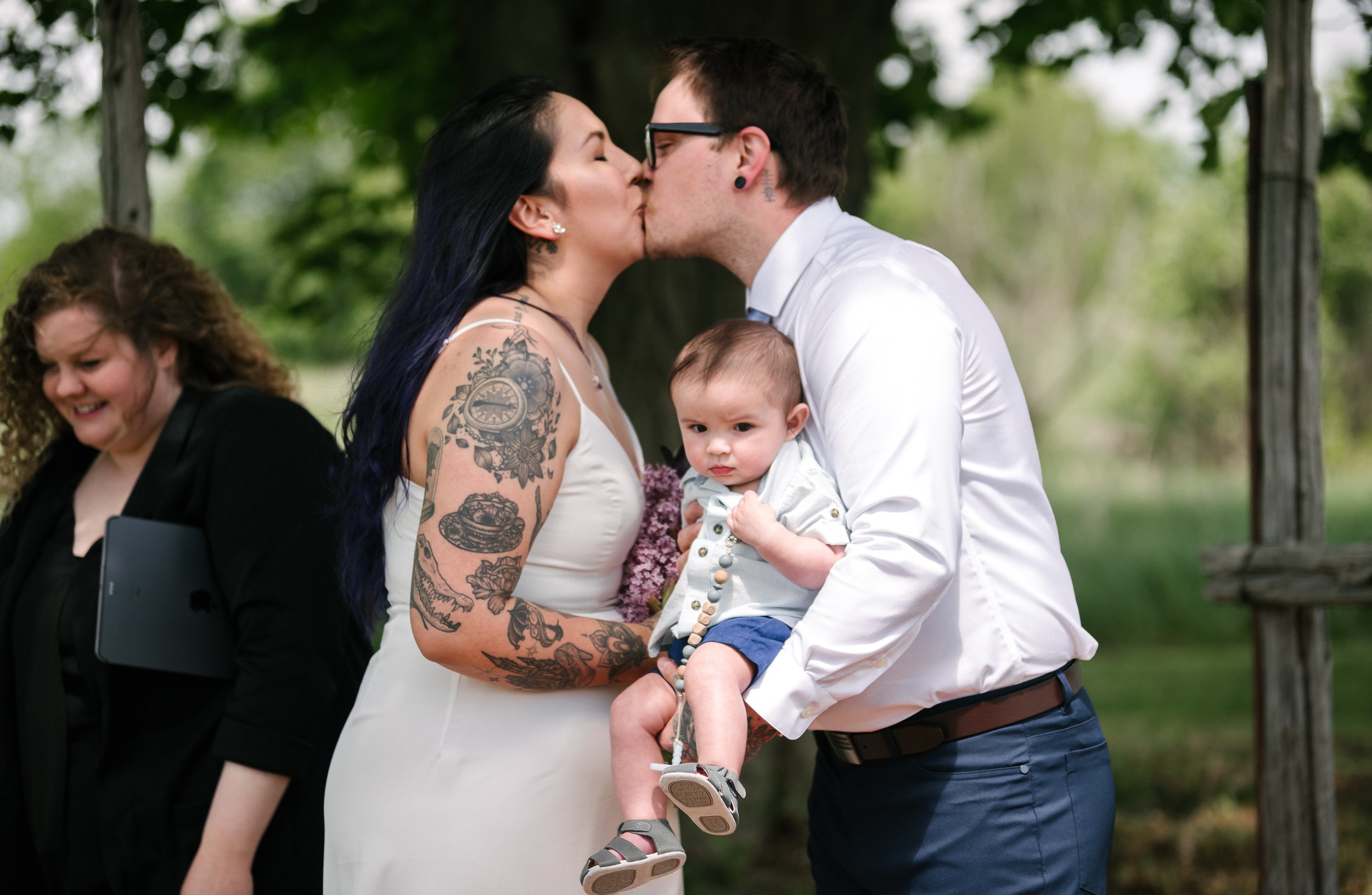 Bride and groom sharing first kiss holding little baby