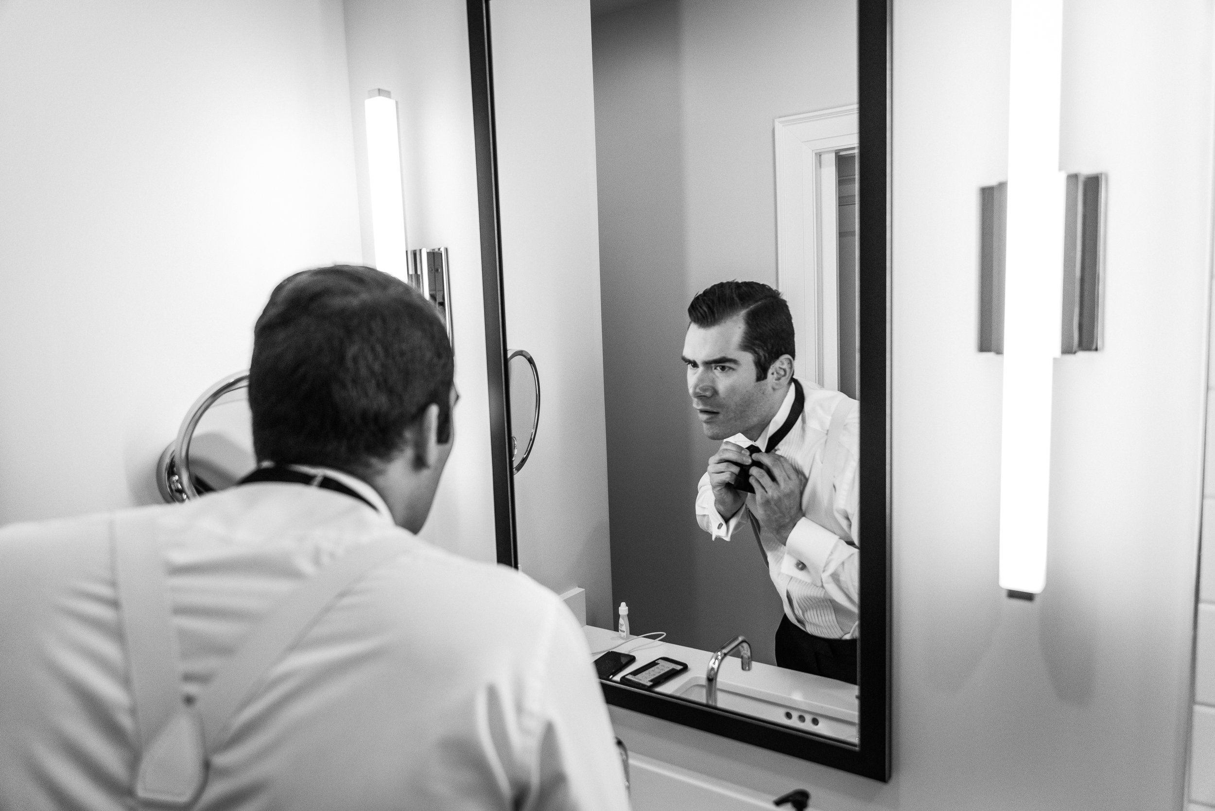 Black and white image of groom looking into the mirror.