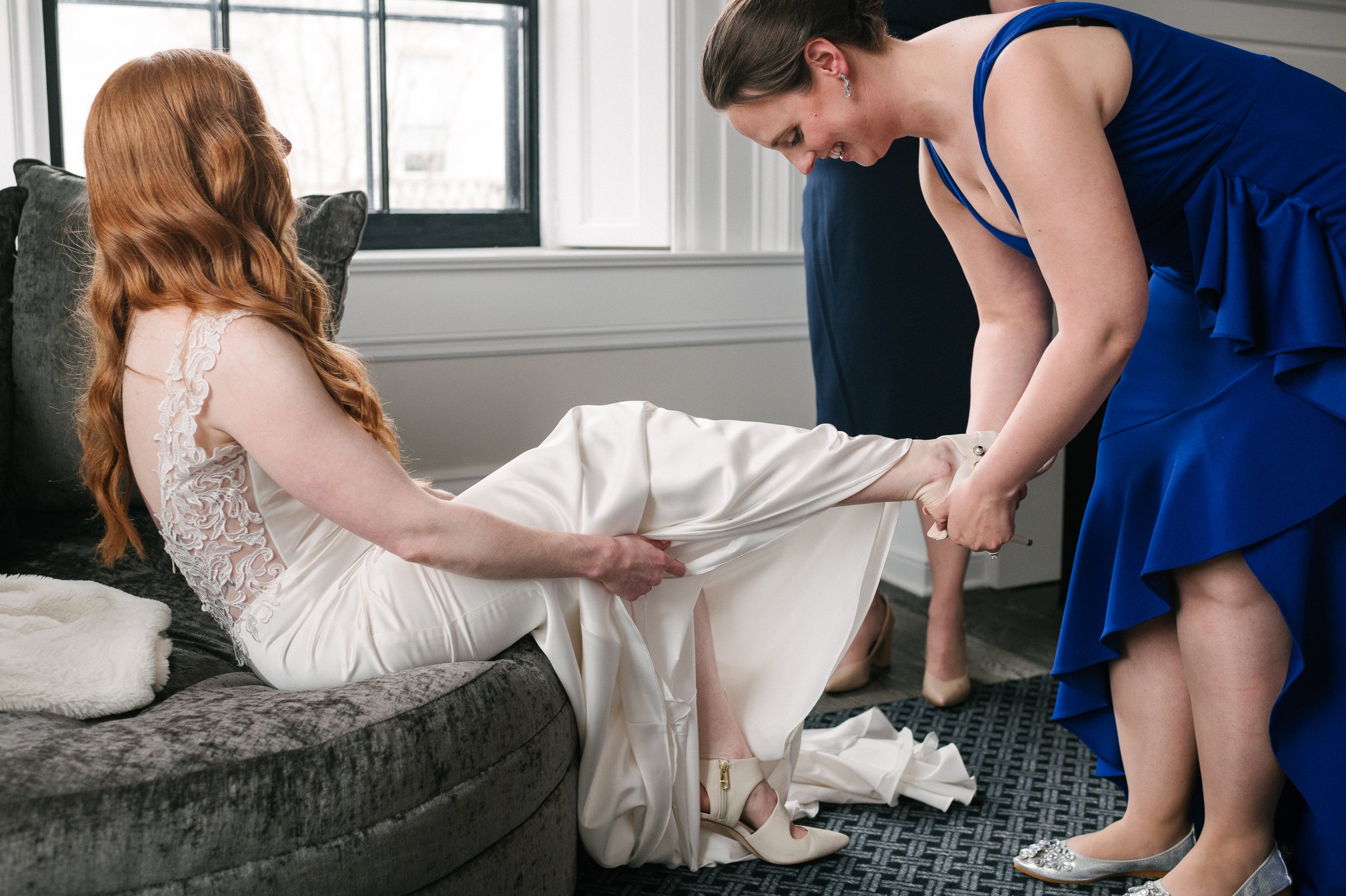 Bridesmaid helping the bride in wearing her dress and sandals