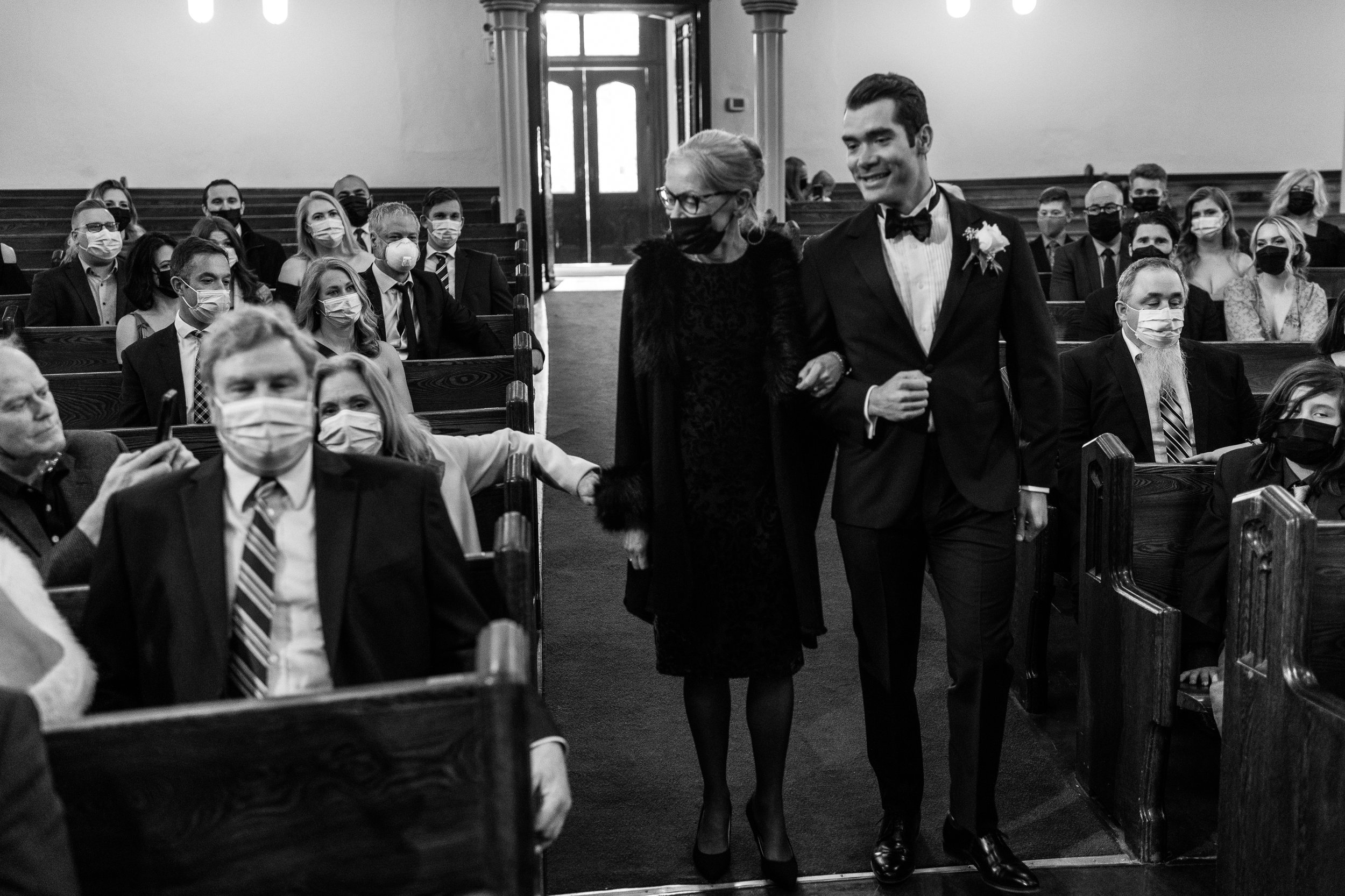 Black and white picture of Groom walking down the aisle with his mother