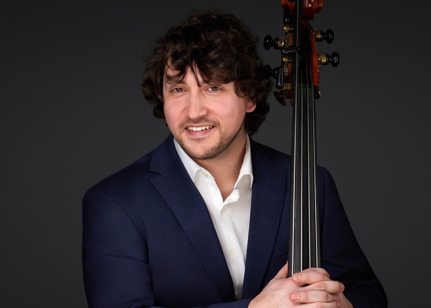 A man wearing a suit smiles with an upright bass