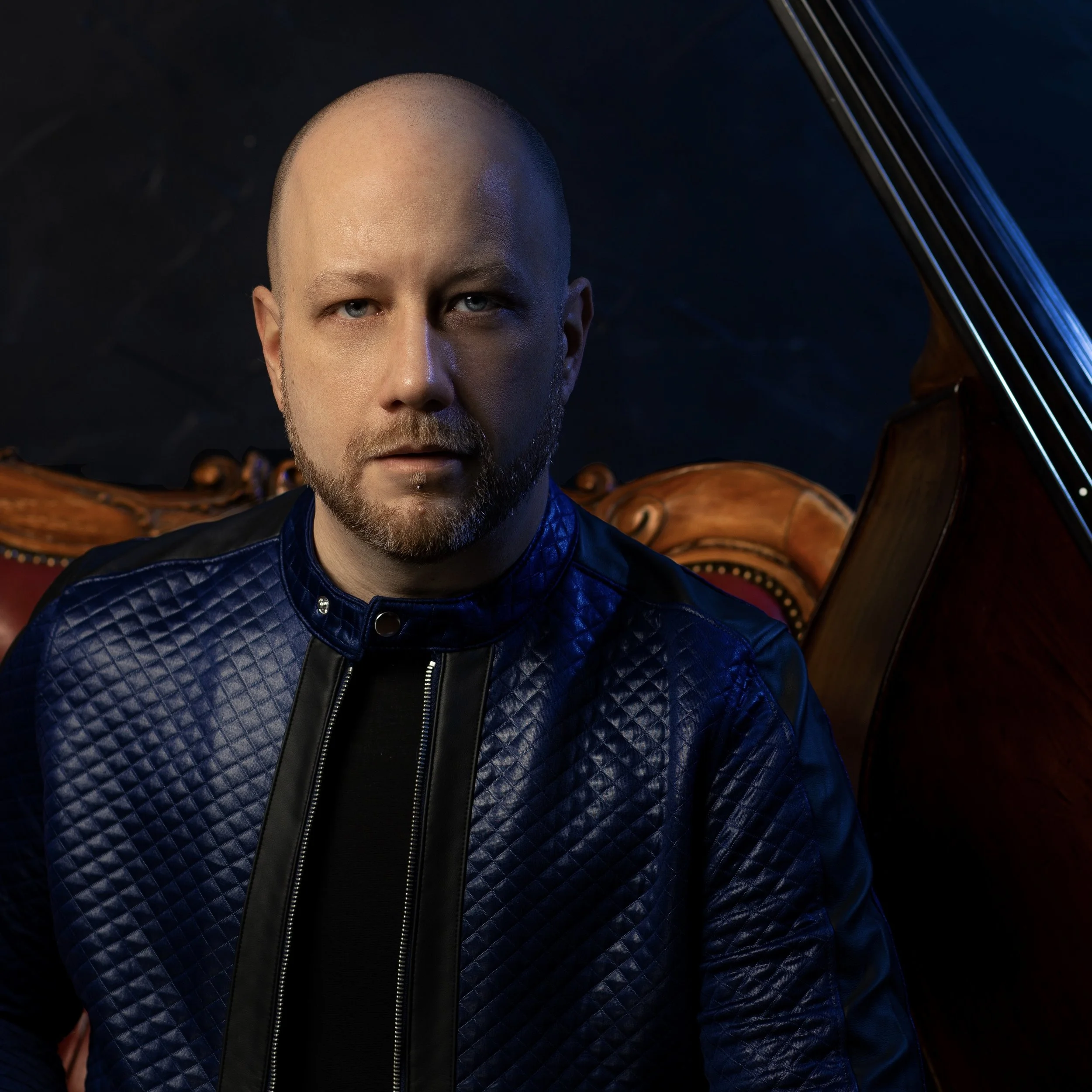 A man appears serious in front of an upright bass