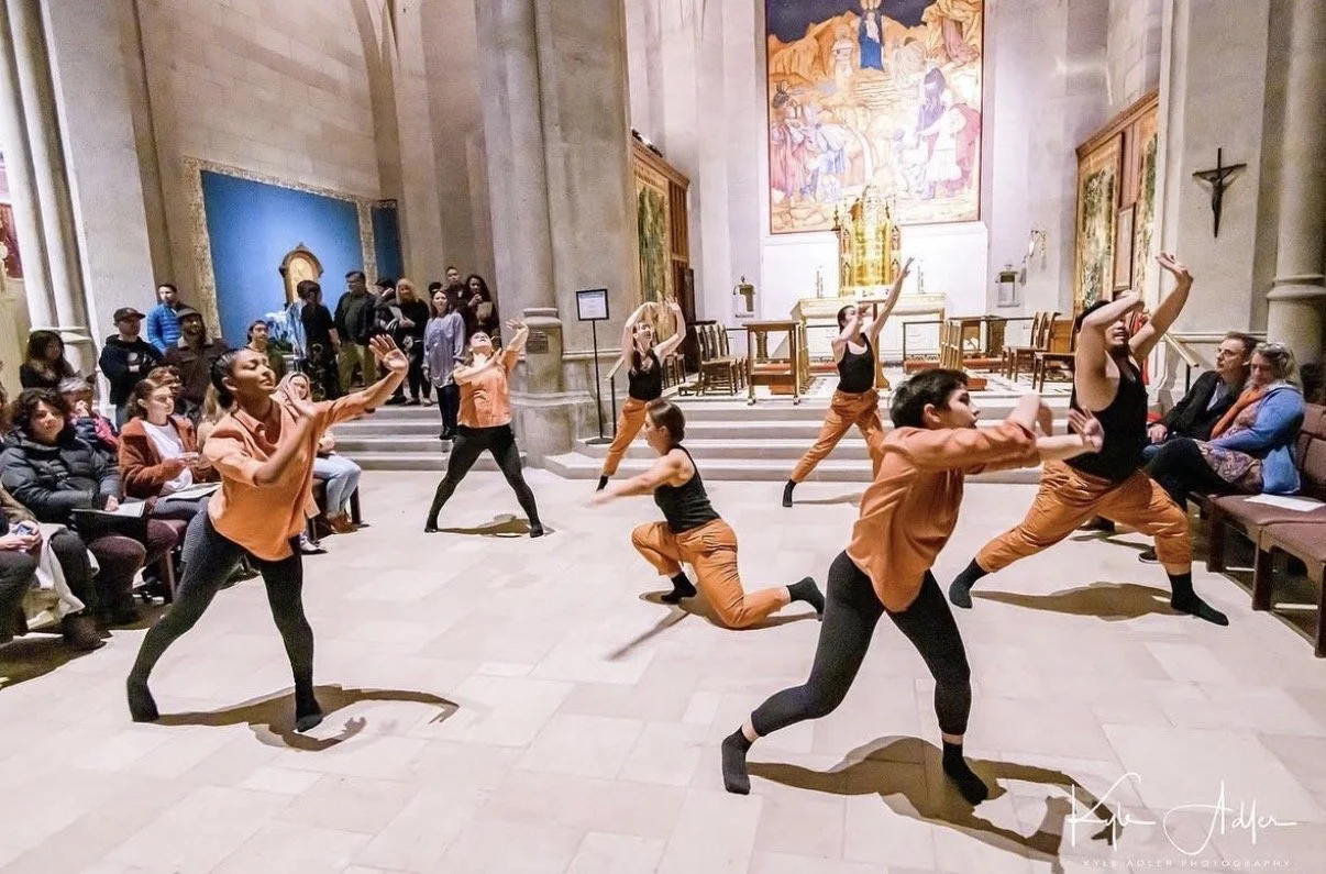 Group of dancers performing in a church, with some audience members seated and others standing, during a dance performance.