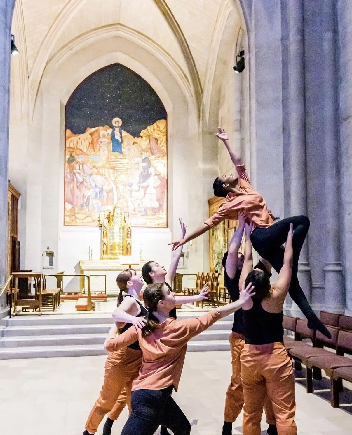 Group of dancers practicing a lift inside a church with an ornate altar and religious painting in the background.